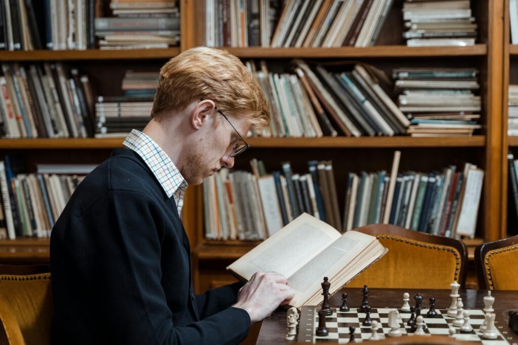 Side view of man reading and playing chess in a library setting.