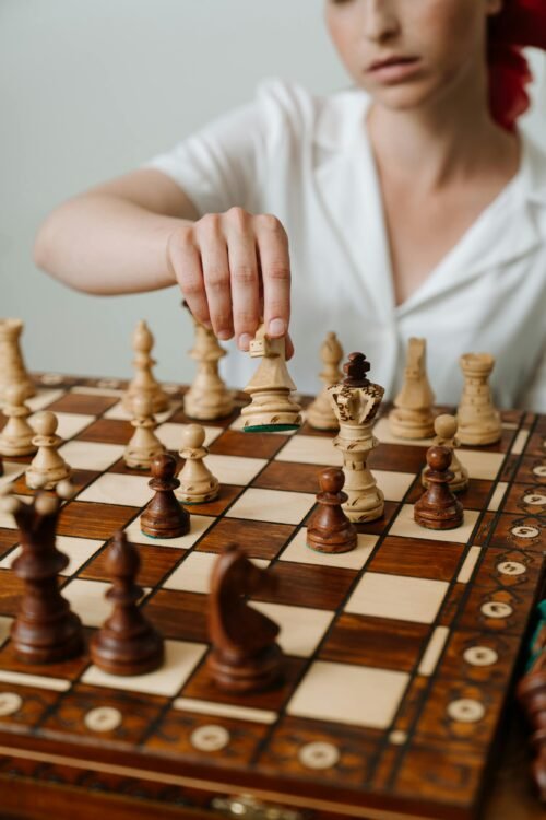 Close-up of a woman's hand making a strategic chess move on a wooden board.