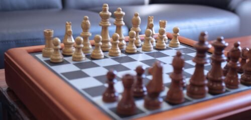 Close-up of a chess game on a wooden chessboard, showcasing strategic gameplay with carved pieces.